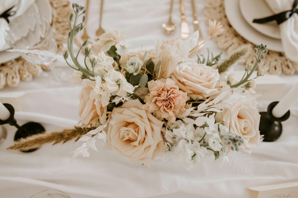 Elegant floral centerpiece featuring soft peach roses, white flowers, and greenery, set on a beautifully arranged wedding table with fine dining elements, enhancing the romantic atmosphere for Las Vegas weddings.